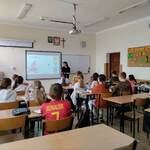 Uczniowie siedzą w ławkach w klasie i patrzą na wyświetlaną prezentację na ekranie przez dziewczynę..jpg