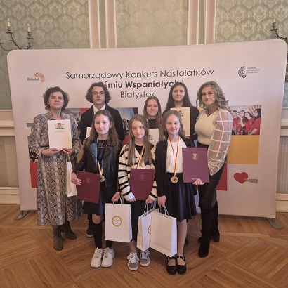 Grupa uczniów stoi razem z dwiema paniami. Wszyscy trzymają dyplomy i papierowe torby..jpg