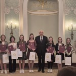 Grupa dziewczynek pozuje do zdjęcia z prezydentem miasta. Dziewczynki trzymają w rękach dyplomy i papierowe torby..jpg