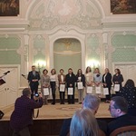 Grupa kobiet stoi na scenie w zabytkowym wnętrzu pałacu.jpg
