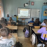 Grupa uczniów siedzi w ławkach w klasie i patrzy na ekran.jpeg