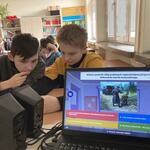 Widok ekranu laptopa na tle uczniów grających na komórkach.jpg