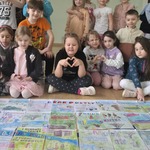 Grupa dzieci siedzi przed duzym kolorowym plakatem.jpg