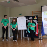 Troje studentów w zielonych koszulkach pokazuje prezentację