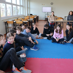 Grupa uczniów siedzi na niebieskiej macie.
