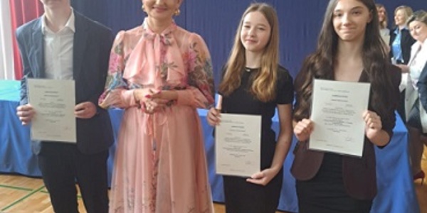 Troje uczniów stoi obok kobiety ubranej w kolorowa sukienkę..jpg