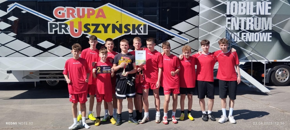 Grupa uczniów ubranych w sportowe stroje stoi na tle baneru..jpg