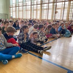 Grupa dzieci siedzi na podłodze hali sportowej..jpg