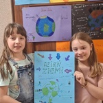 Dwie dziewczynki trzymają plakat w rękach na tle drzwi wyklejonych plakatami.jpg