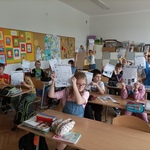 Grupa dzieci pozuje w klasie do zdjęcia trzymając karty pracy w górze w rękach..jpg