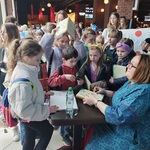 Grupa dzieci stoi przy pani podpisującej książki.jpg