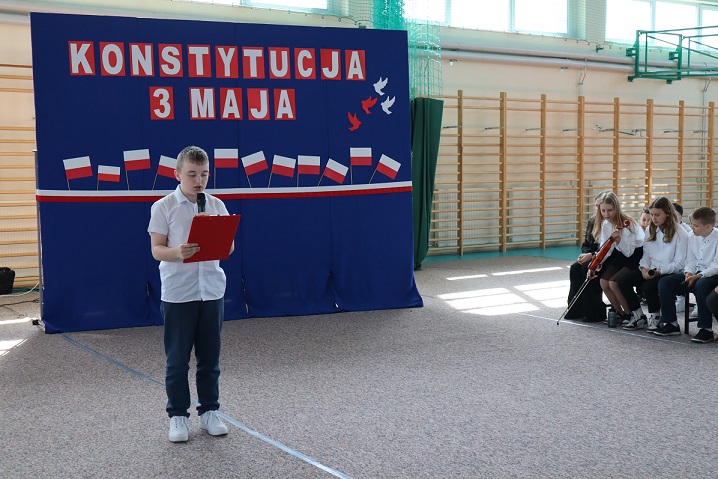 chłopiec czyta tekst na tle niebieskiej tablicy z biało-czerwonymi napisami.JPG