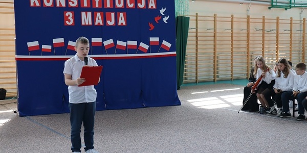 chłopiec czyta tekst na tle niebieskiej tablicy z biało-czerwonymi napisami.JPG