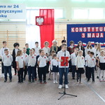 Grupa uczniów ubrana w stroje galowe i przypiete kotyliony stoi przy tablicy z biało-czerwonymi napisami.JPG
