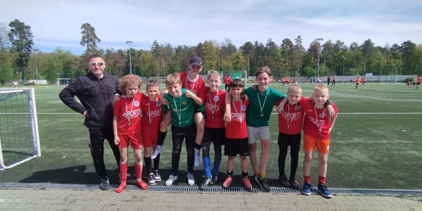 Grupa chłopców w czerwonych strojach sportowych pozuje razem z trenerem na boisku do piłki nożnej..jpg