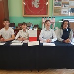 Czterech chłopców siedzi przy stole z biało-czerwoną urną.jpg