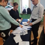 Troje uczniów rozkłada kartki na stole.jpg