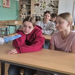 Dwie dziewczyny patrzą na jaszczurkę trzymaną na ręce w niebieskiej rękawiczce.jpg