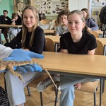 Uczniowie patrzą na gekona trzymanego na ręce w niebieskiej rękawiczce.jpg