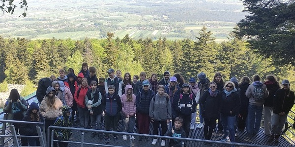 Grupa młodzieży i osób dorosłych stoi na kładce na tle panoramy na zielone pola i lasy.jpg