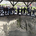 Grupa młodzieży i osób dorosłych stoi przy poręczy z wykopaliskami.jpg