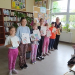 Grupa dzieci pozuje z panią do zdjęcia w bibliotece.  W rękach trzymają dyplomy.jpg