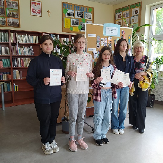 Cztery uczennice pozują do zdjęcia w bibliotece.  W rękach trzymają dyplomy.jpg