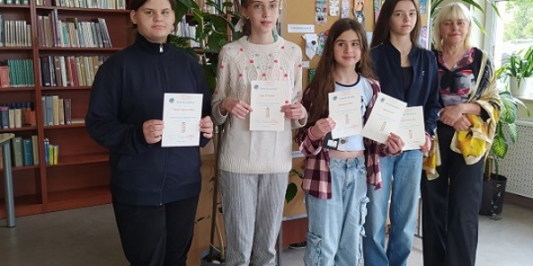 Cztery uczennice pozują do zdjęcia w bibliotece.  W rękach trzymają dyplomy.jpg