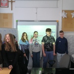 Grupa uczniów stoi na tle wyświetlanego filmu na tablicy multimedialnej..jpg