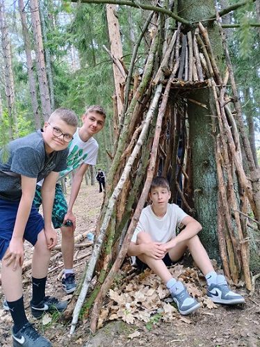 Trzech chłopaków przy szłasie z patyków w lesie.jpg