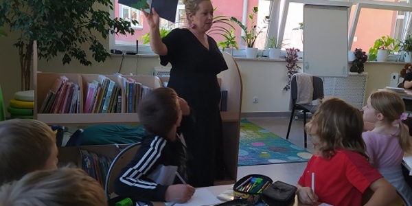 Nauczyciel bibliotekarz pokazuje uczniom ksiązkę.jpg