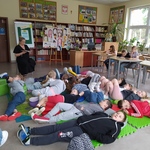 Nauczyciel czyta ksiązkę uczniom leżącym na podłodze na matach.jpg