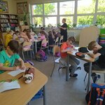 Nauczycielka czyta uczniom które  siedzą przy stolikach w biboliotece.jpg