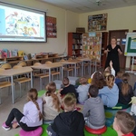 Nauczycielka stoi i opowiada o książce dzieciom_ które siedzą na podłodze w biboliotece.jpg