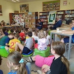 Pani czyta dzieciom_ które leżą lub siedzą na podłodze w bibliotece.jpg