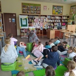 Pani Dyrektor pokazjue bohaterów książki dzieciom_ które leżą lub siedzą na podłodze w biboliotece.jpg