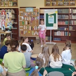 Uczennica czyta tekst konkursowy dzieciom_ które siedzą na podłodze w biboliotece..jpg