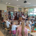 Uczennica czyta tekst na kartce dzieciom_ które siedzą na podłodze w biboliotece..jpg