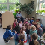 Uczennica starszej klasy czyta dzieciom w bibliotece.jpg