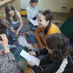 Uczennice siedzą na podłodze  i trzymają w rękach kartki.jpg