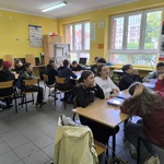 Grupa uczniów siedzi w sali przy stolikach.jpg