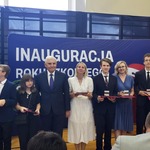 Grupa elegancko ubranych osób pozuje do zdjęcia na tle napisu na granatowym tle