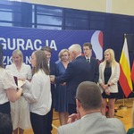 Mężczyzna elegancko ubrany wręcza medale osobom stojącym w rzędzie.