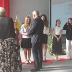 Mężczyzna w garniturze wręcza dyplomy dziewczynom stojącym na plastikowych czerwonych sercach..jpg
