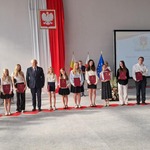 Grupa elegancko ubranych uczniów pozuje do zdjęcia z czerwonymi dyplomami w rękach.jpg