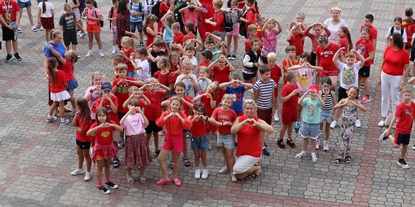 Grupa dzieci ubrana na czerwono pozuje do zdjęcia. Dzieci pokazują z rąk serca..jpg