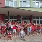 Grupa dzieci ubrana na czerwono pozuje do zdjęcia przy szkole. Dzieci pokazują z rąk serca..jpg