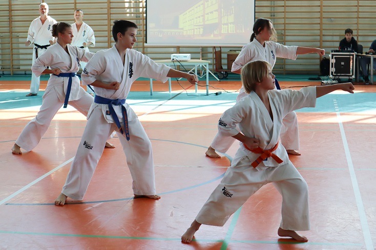 Sportowcy ubrani w białe kimona pokazują chwyty w karate na hali sportowej..jpg