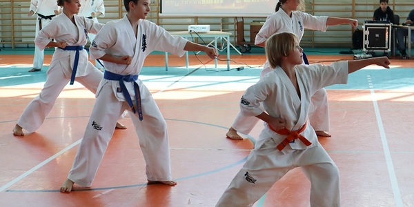 Sportowcy ubrani w białe kimona pokazują chwyty w karate na hali sportowej..jpg