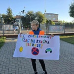 Na chodniku przed ogrodzeniem stoi chłopiec o blond włosach i trzyma plakat z kolorowym napisem.jpg